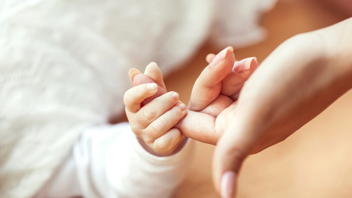 baby holding mom's finger istock