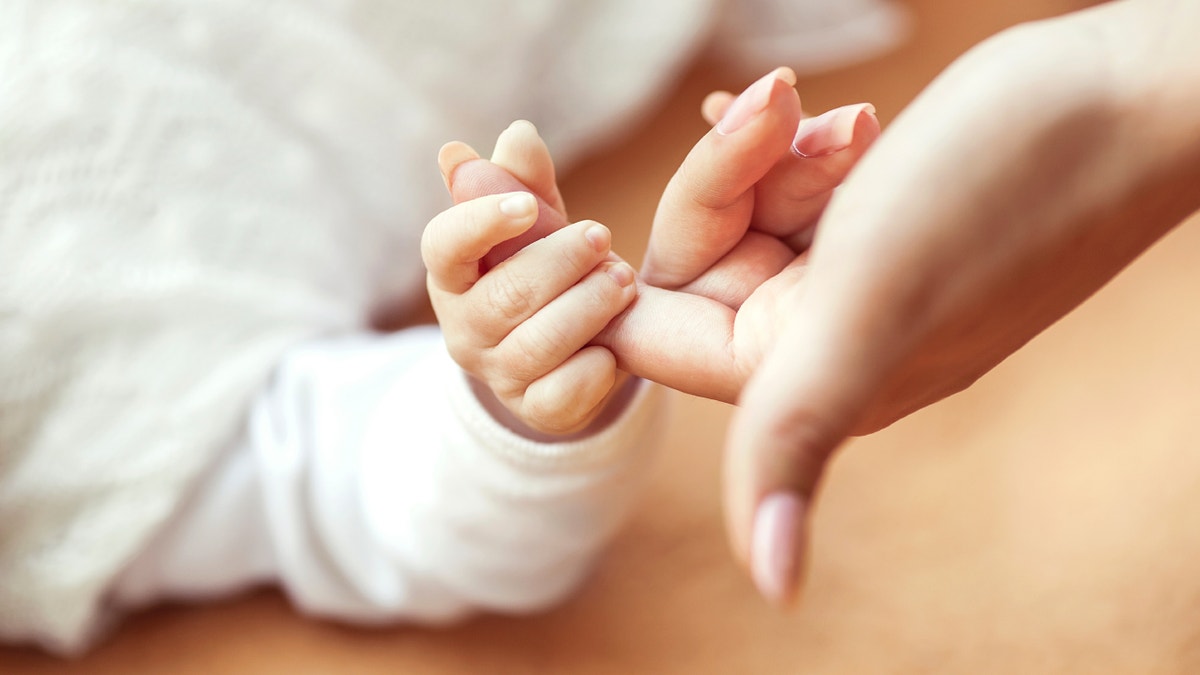 baby holding mom's finger istock