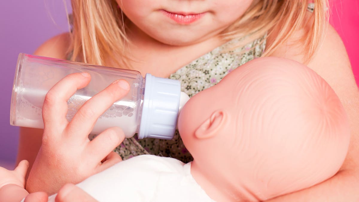 Girl feeds baby doll bottle