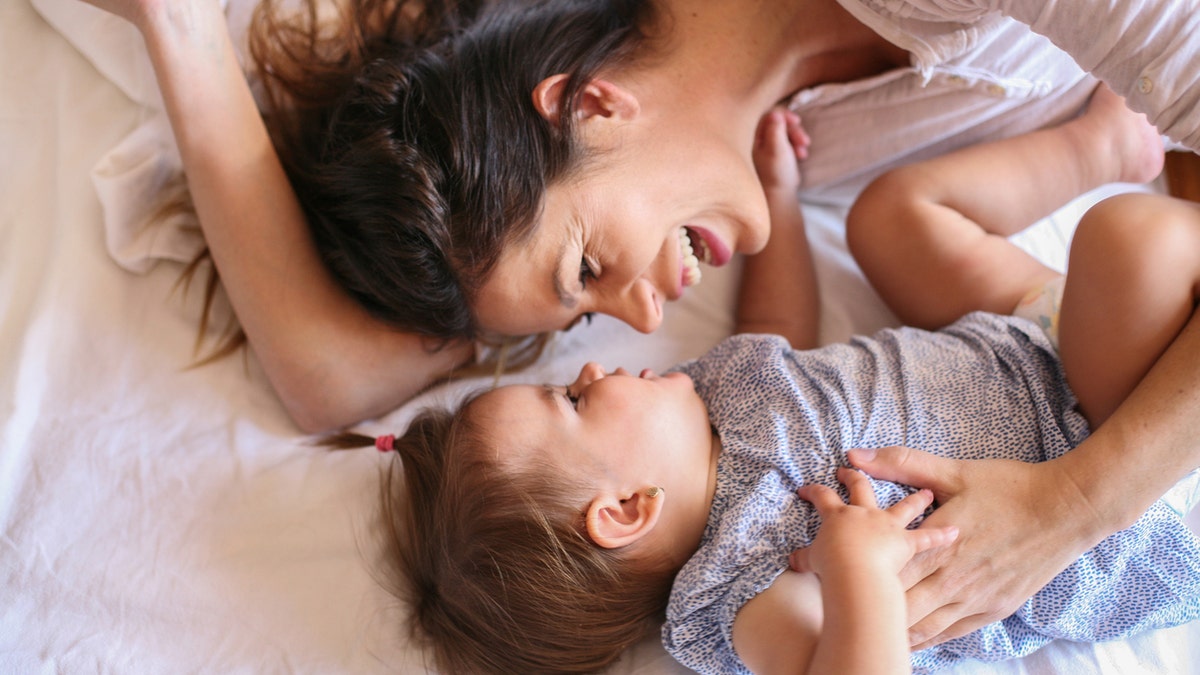 Young mother playing with her baby girl playing in bed. Space for copy.