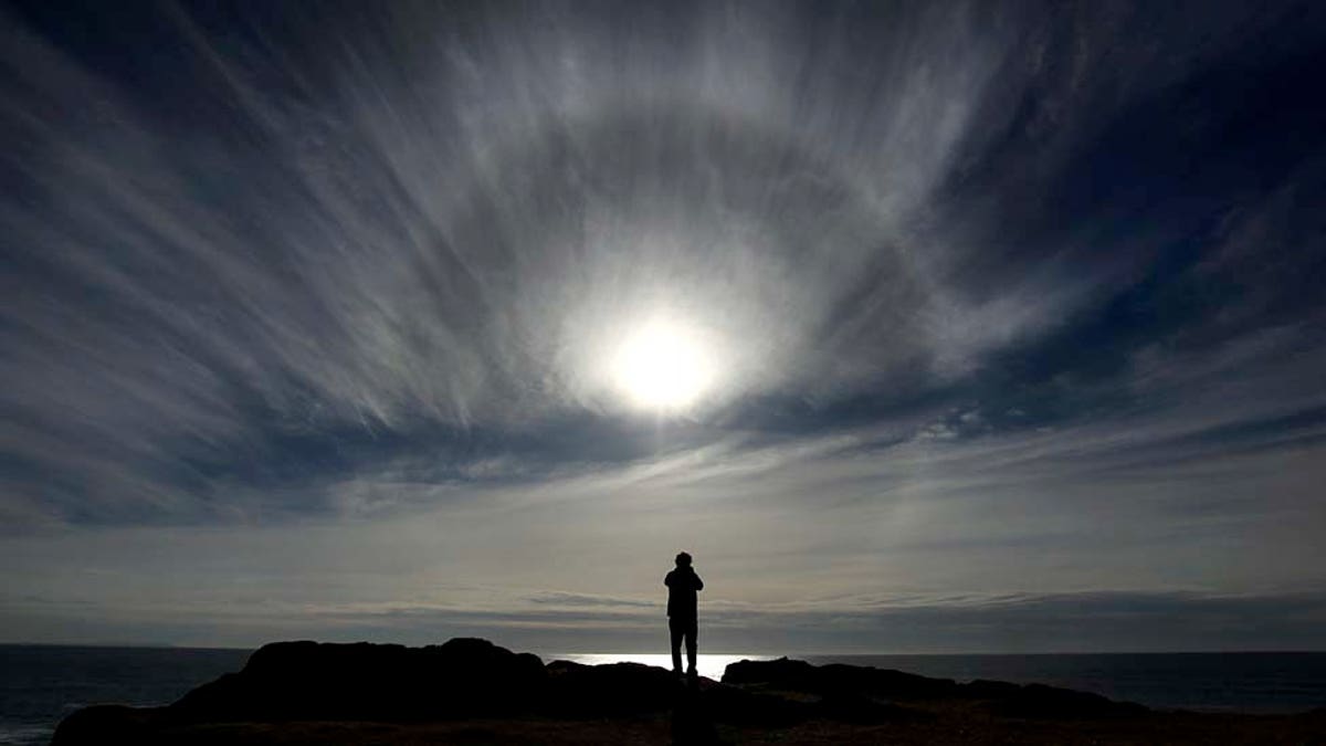 Thomas Mullin of Mill Valley, Calif. gets a last look at the sun from Bodega Head, Thursday Dec. 16, 2010 in Bodega Bay Calif., as the first in a series of large Pacific storms move inland, bringing a promise of heavy precipitation and high winds. The thin high clouds ahead of the front produce a halo containing millions of tiny ice crystals which take on an elongated hexagonal shape, refracting the light. (AP Photo/Kent Porter, Santa Rosa Press Democrat)