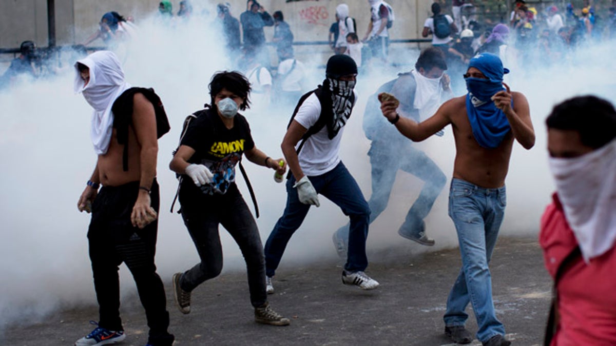 A group of masked men run for cover after riot police launched tear gas in Caracas, Venezuela, Saturday, Feb. 22, 2014. After an opposition rally broke up in the late afternoon, in a pattern that has been seen in past demonstrations about 1,000 stragglers erected barricades of trash and other debris and threw rocks and bottles at police and National Guardsmen. The troops responded with volleys of tear gas to prevent the students from reaching a highway and blocking traffic. (AP Photo/Rodrigo Abd