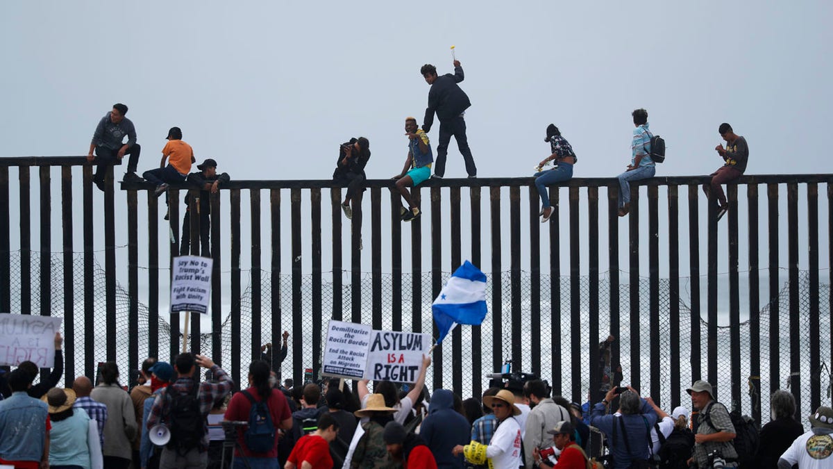 People climb the border wall fence as a caravan of migrants and supporters reached the United States-Mexico border near San Diego, California, U.S., April 29, 2018. REUTERS/Mike Blake - HP1EE4T1D57HL