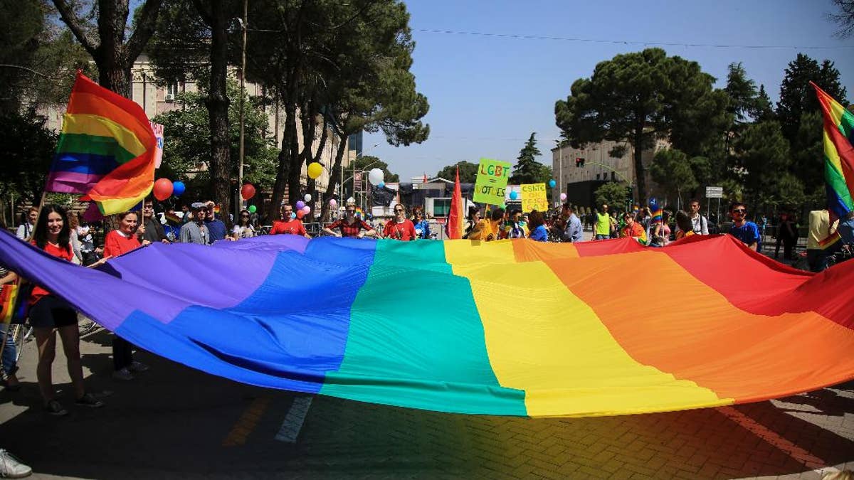 Participants of the Gay Pride Parade hold a rainbow flag during a rally held without any disturbances, while the country's political opposition prepared for an unrelated national protest in the capital, in Tirana, Saturday, May 13, 2017. Scores of bikers with multi-colored balloons and flags rode passing past a tent pitched by the opposition in front of Prime Minister Edi Rama's office urging the government to take anti-discriminatory measures and pass two draft laws on same-sex marriage and recognition of trans-gender people. (AP Photo/Hektor Pustina)