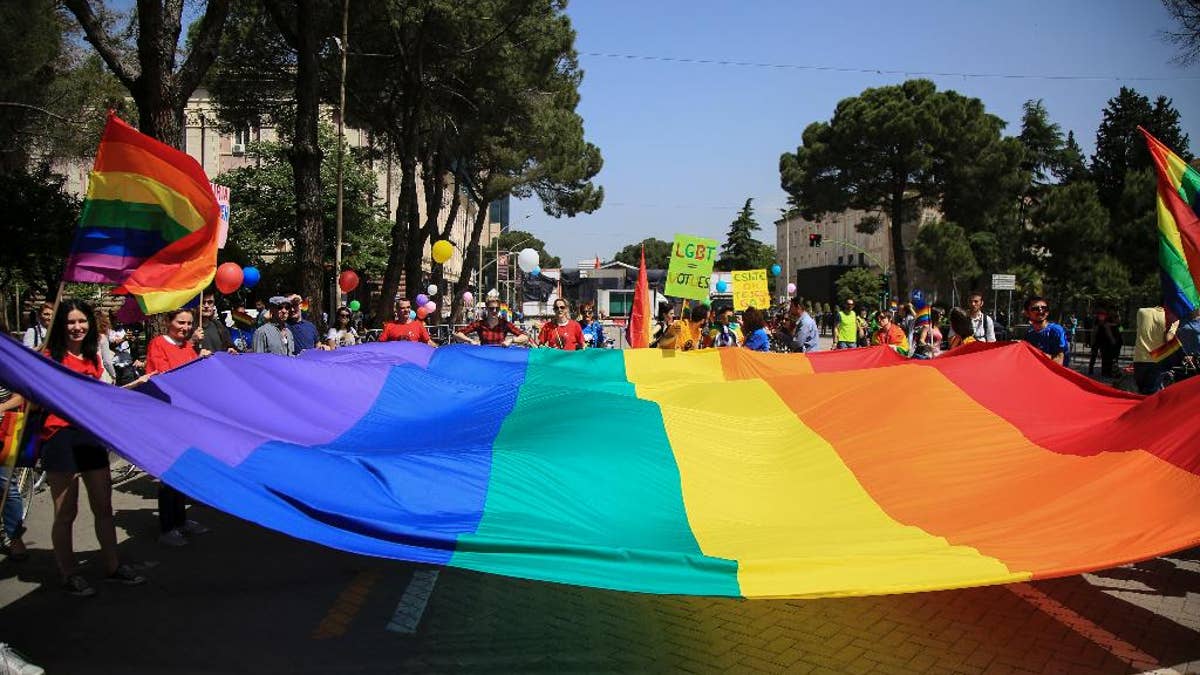 Participants of the Gay Pride Parade hold a rainbow flag during a rally held without any disturbances, while the country's political opposition prepared for an unrelated national protest in the capital, in Tirana, Saturday, May 13, 2017. Scores of bikers with multi-colored balloons and flags rode passing past a tent pitched by the opposition in front of Prime Minister Edi Rama's office urging the government to take anti-discriminatory measures and pass two draft laws on same-sex marriage and recognition of trans-gender people. (AP Photo/Hektor Pustina)