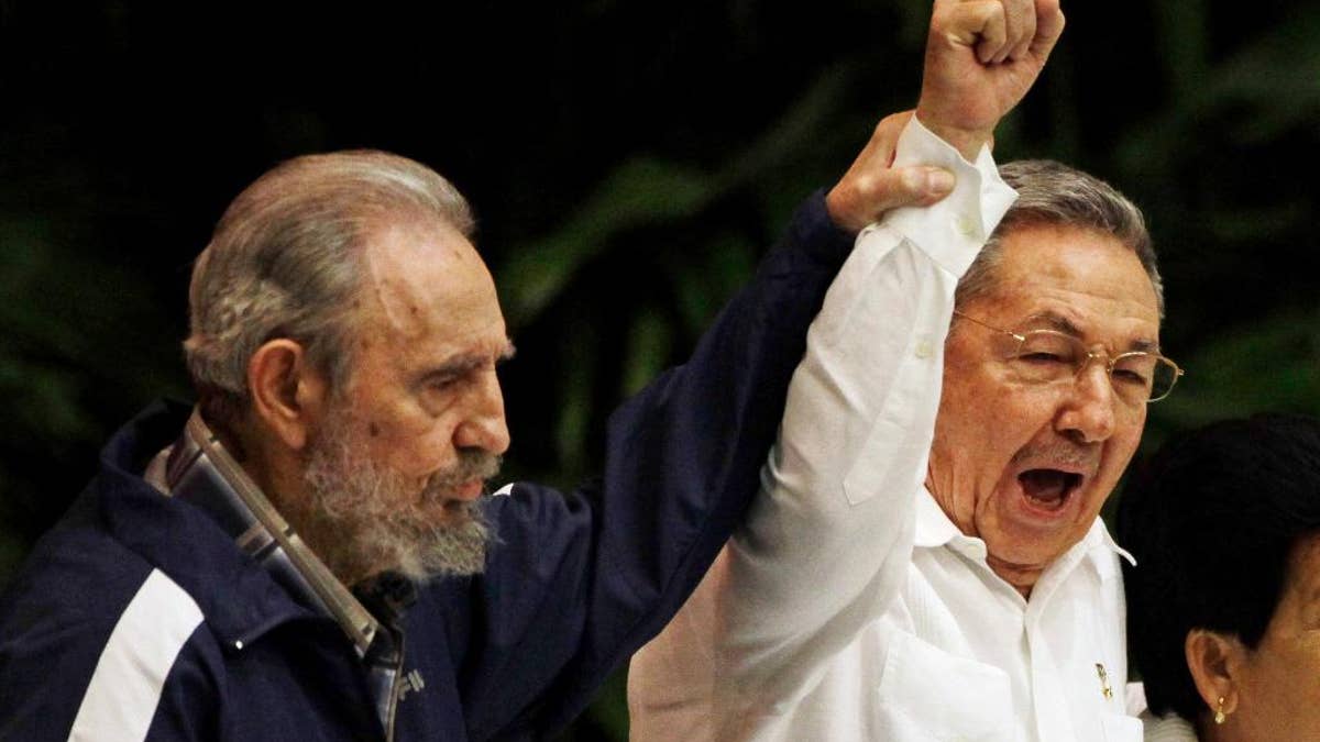 Fidel Castro, left, raises his brother's hand, Cuba's President Raul Castro, center, as they sing the anthem of international socialism in Havana, Cuba.