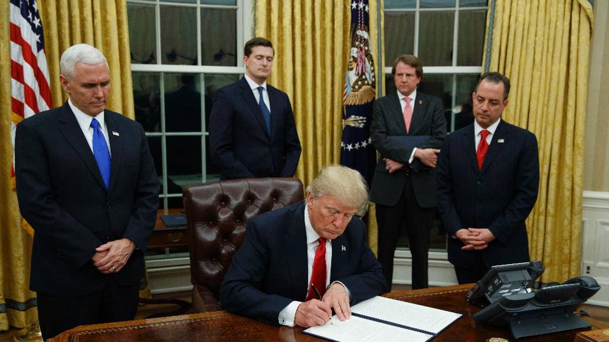 FILE - In this Jan. 20, 2017, file photo,President Donald Trump, flanked by Vice President Mike Pence and Chief of Staff Reince Priebus, signs his first executive order on health care in the Oval Office of the White House in Washington. After years of objecting to President Barack Obama’s use of executive power to work around Congress, President Donald Trump and Republicans allies have all-but abandoned their public complaints about checks-and-balances and embraced the go-it-alone strategy to fast-track their dismantling President Barack Obama's policies. (AP Photo/Evan Vucci, File)