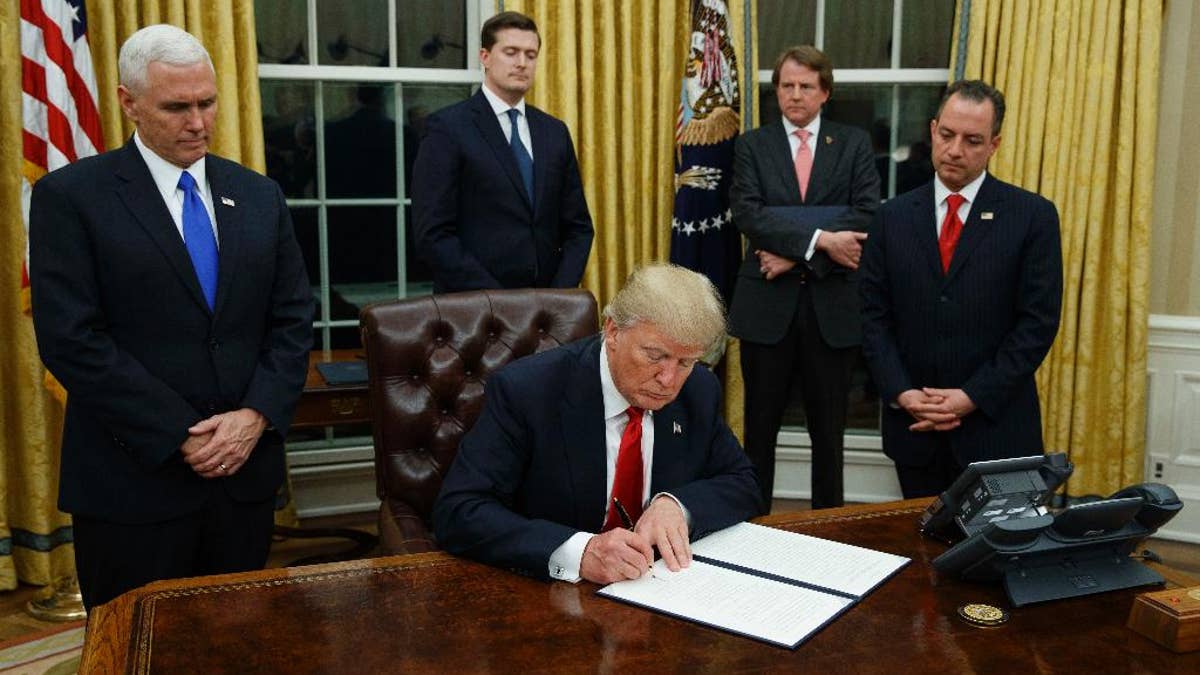 FILE - In this Jan. 20, 2017, file photo,President Donald Trump, flanked by Vice President Mike Pence and Chief of Staff Reince Priebus, signs his first executive order on health care in the Oval Office of the White House in Washington. After years of objecting to President Barack Obama’s use of executive power to work around Congress, President Donald Trump and Republicans allies have all-but abandoned their public complaints about checks-and-balances and embraced the go-it-alone strategy to fast-track their dismantling President Barack Obama's policies. (AP Photo/Evan Vucci, File)