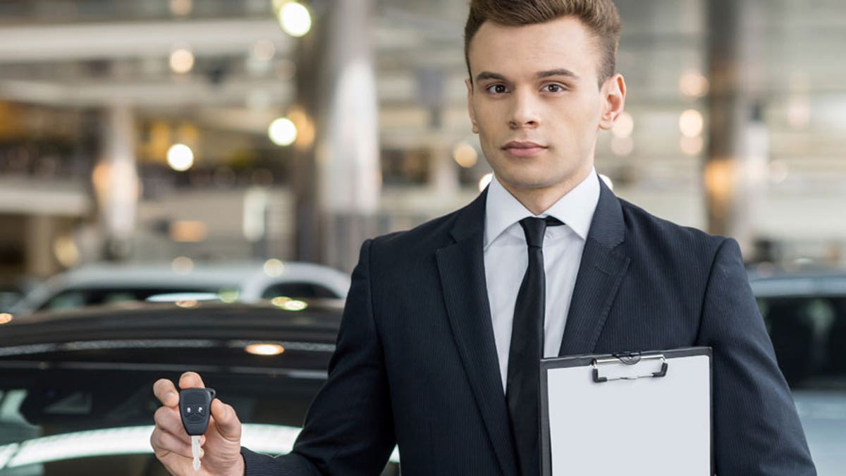 Here is your key! Confident young classic car salesman standing at the dealership and holding a key