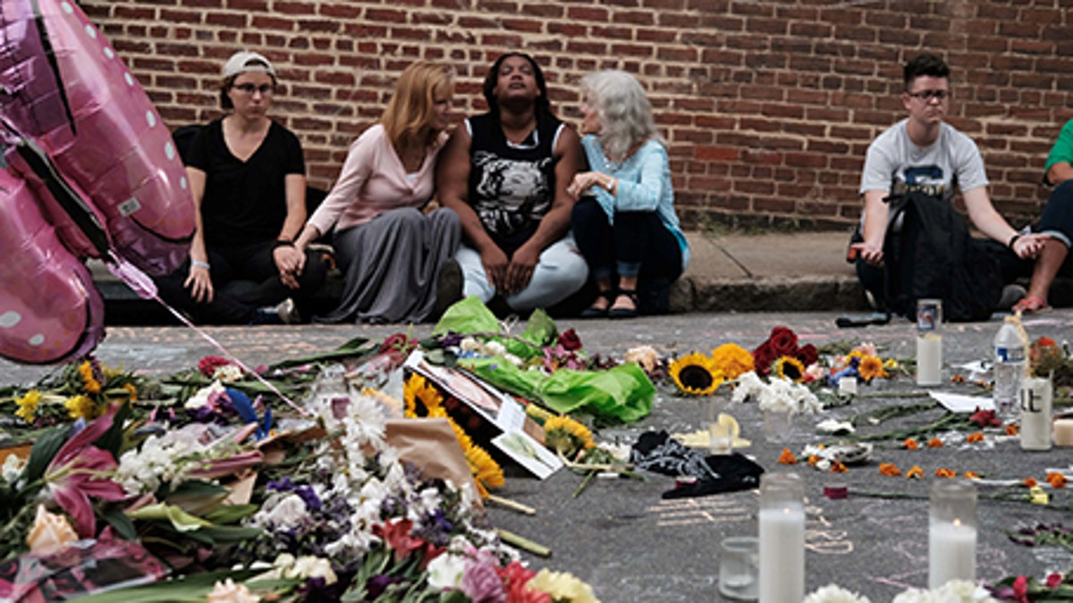 Women sit by an impromptu memorial of flowers commemorating the victims at the scene of the car attack on a group of counter-protesters during the 