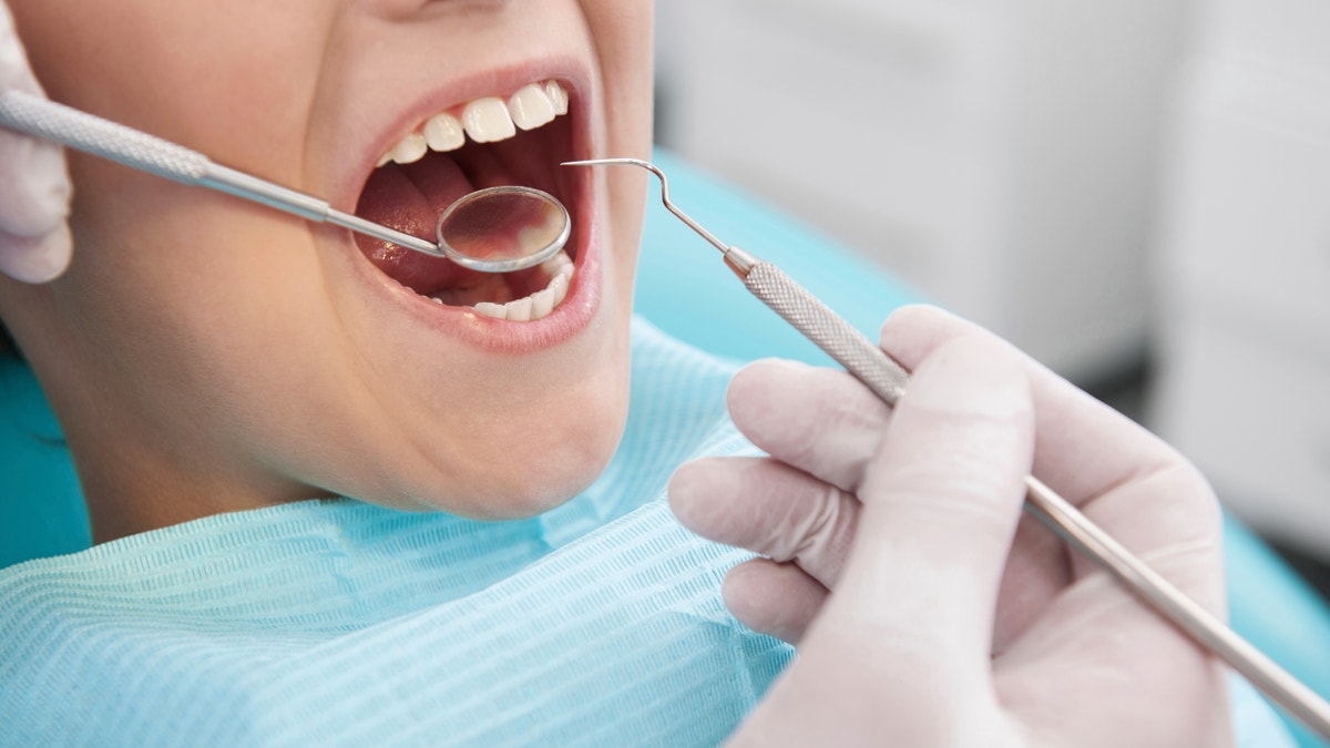 Little boy sitting at the chair at the dental office while doctor examining teeth