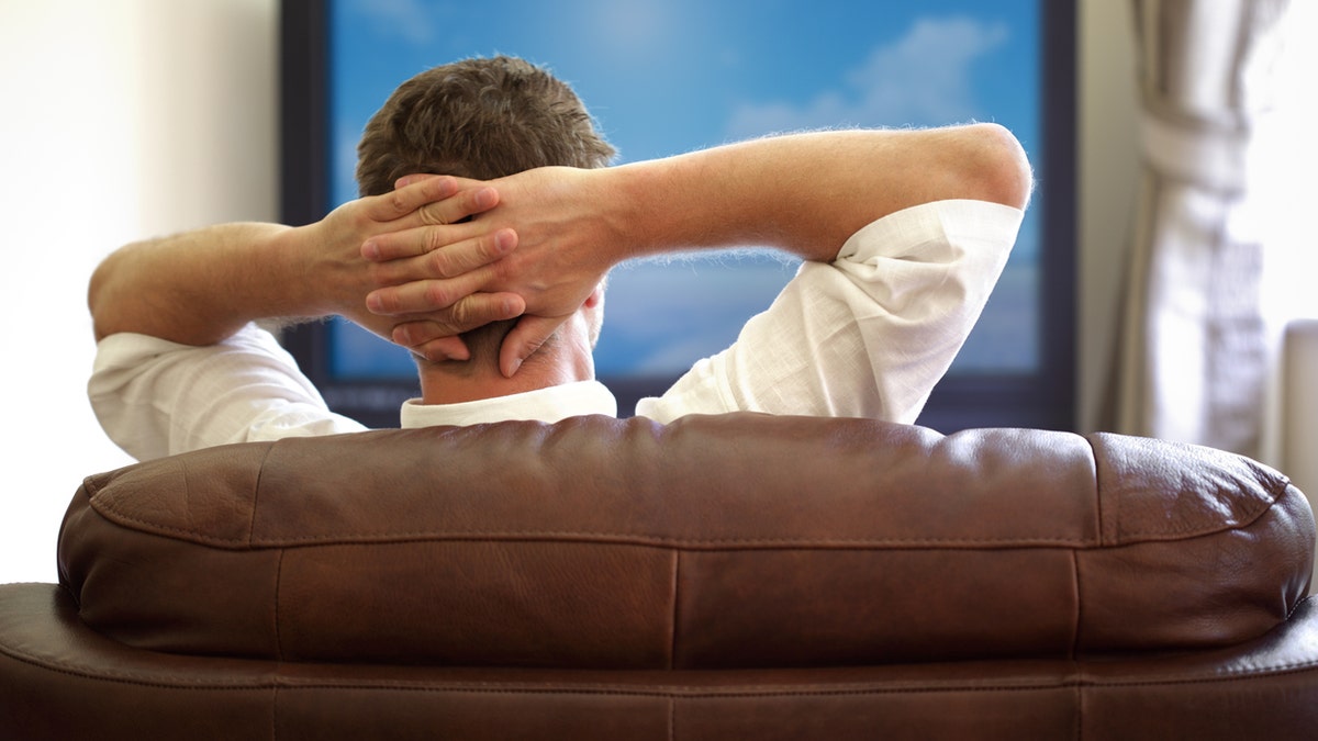 Man sitting on a sofa watching tv with hands folded behind his headPlease see similar picture from my portfolio: