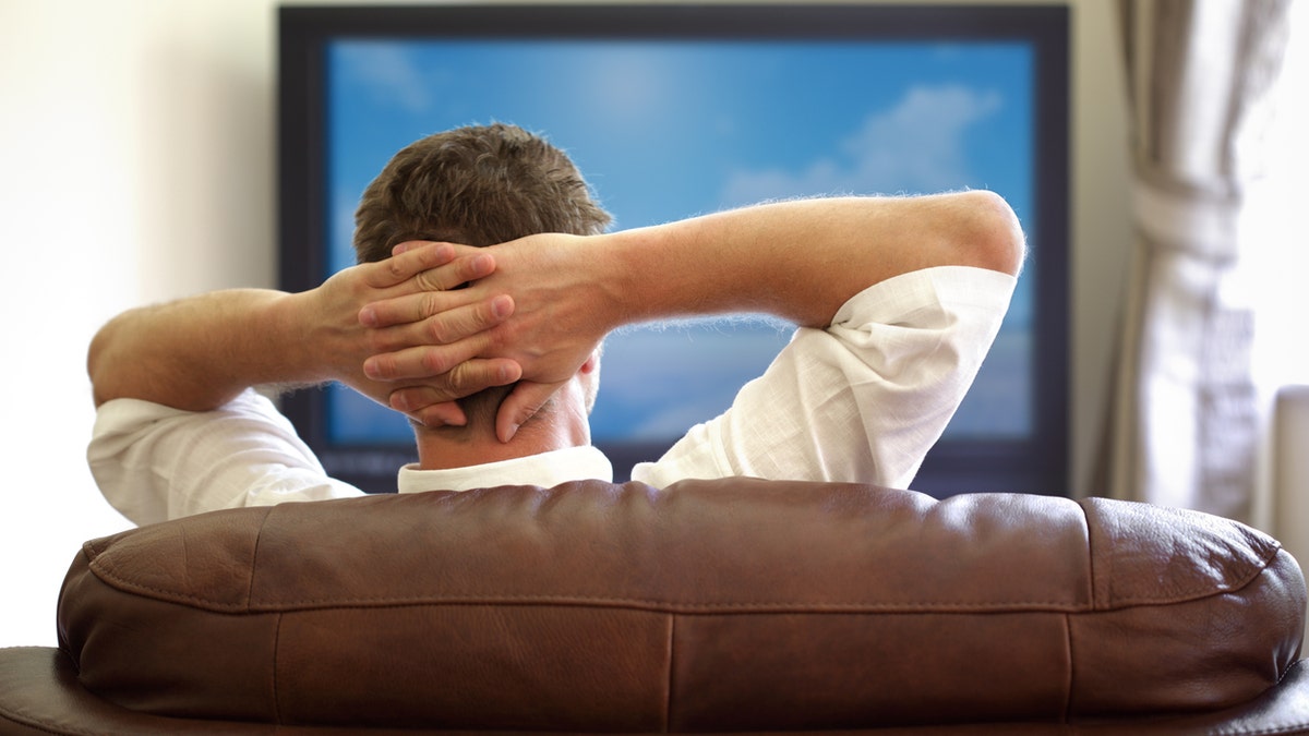 Man sitting on a sofa watching tv with hands folded behind his headPlease see similar picture from my portfolio: