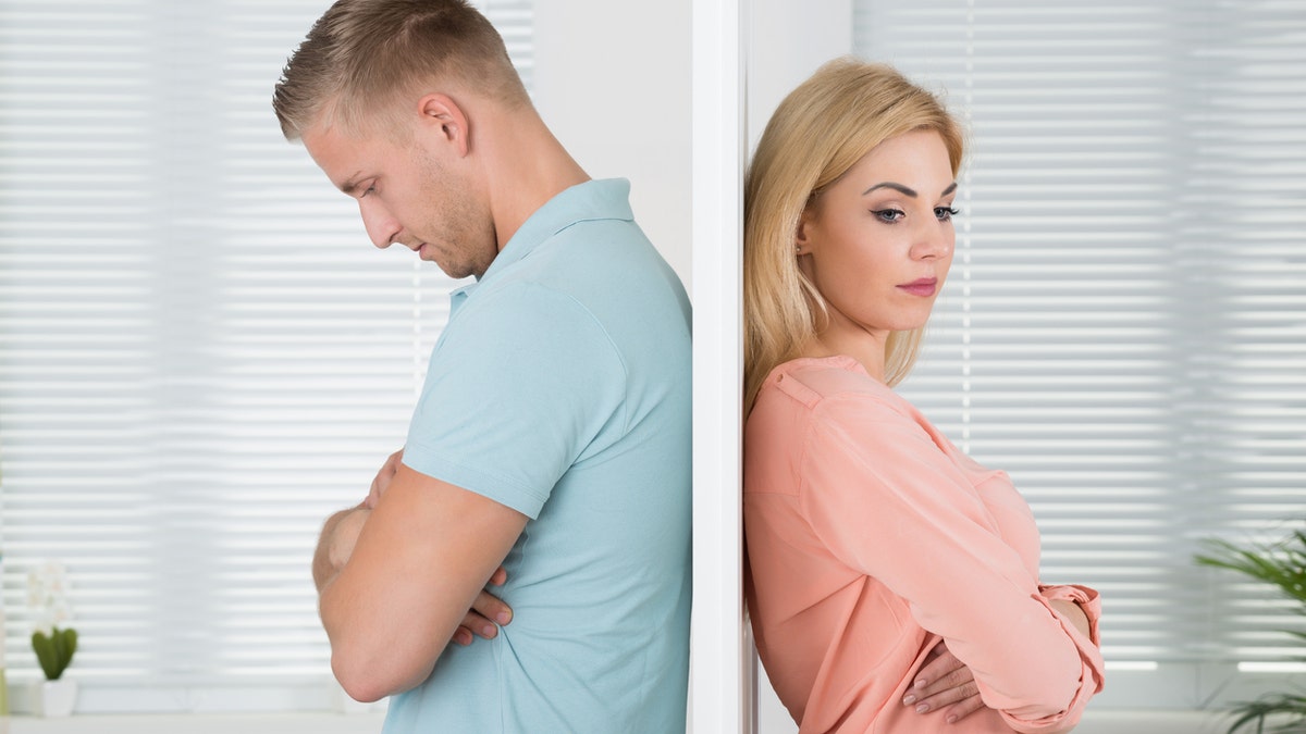 Side view of an unhappy young couple standing back to back at home