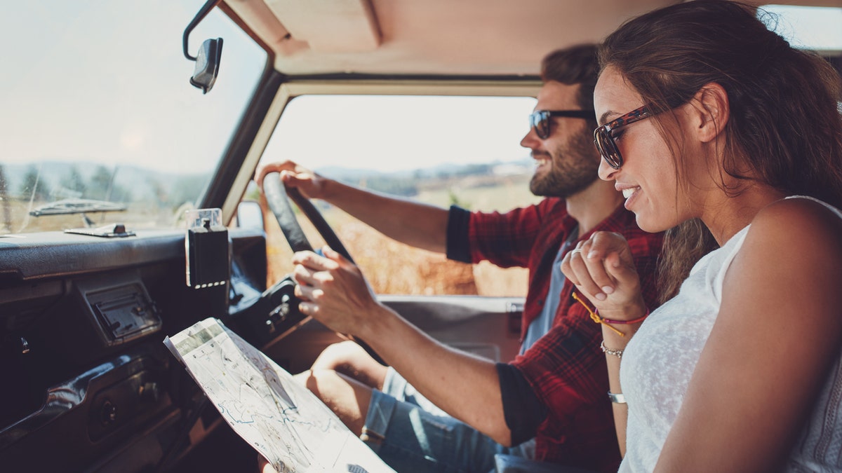 Side view of young couple using a map on a roadtrip for directions. Young man and woman reading a map while sitting in a car.