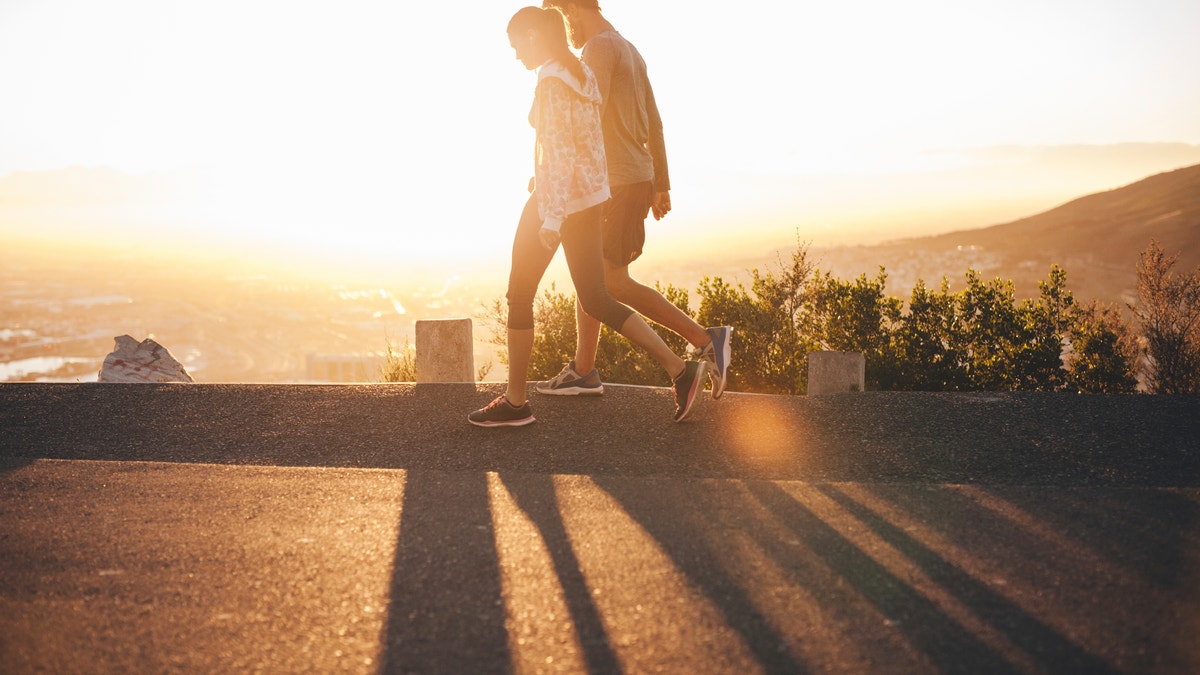 Couple walk along road at sunrise. Couple talking a walk on hillside road with bright sunlight.