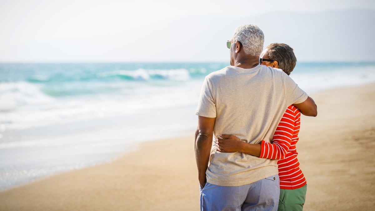 Senior African American couple embracing at sandy beach. 