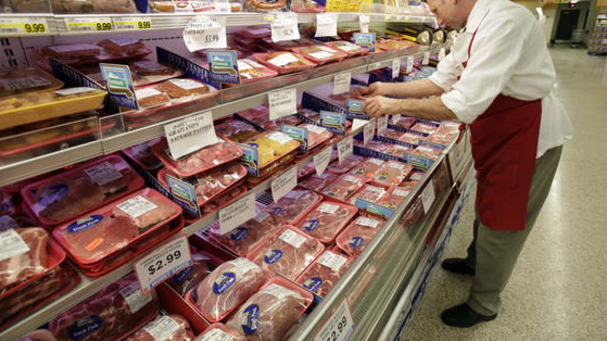 A butcher looks at several cuts of meat at a grocery store. 