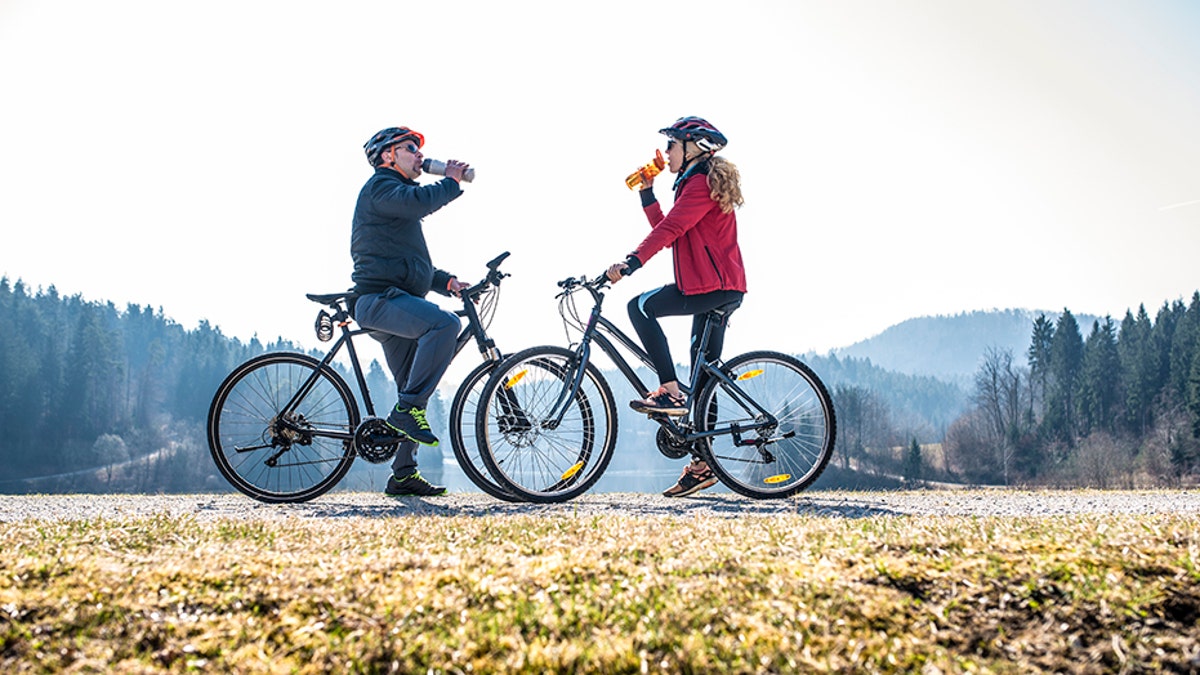 A couple cycling outdoors and taking a break to drink some water