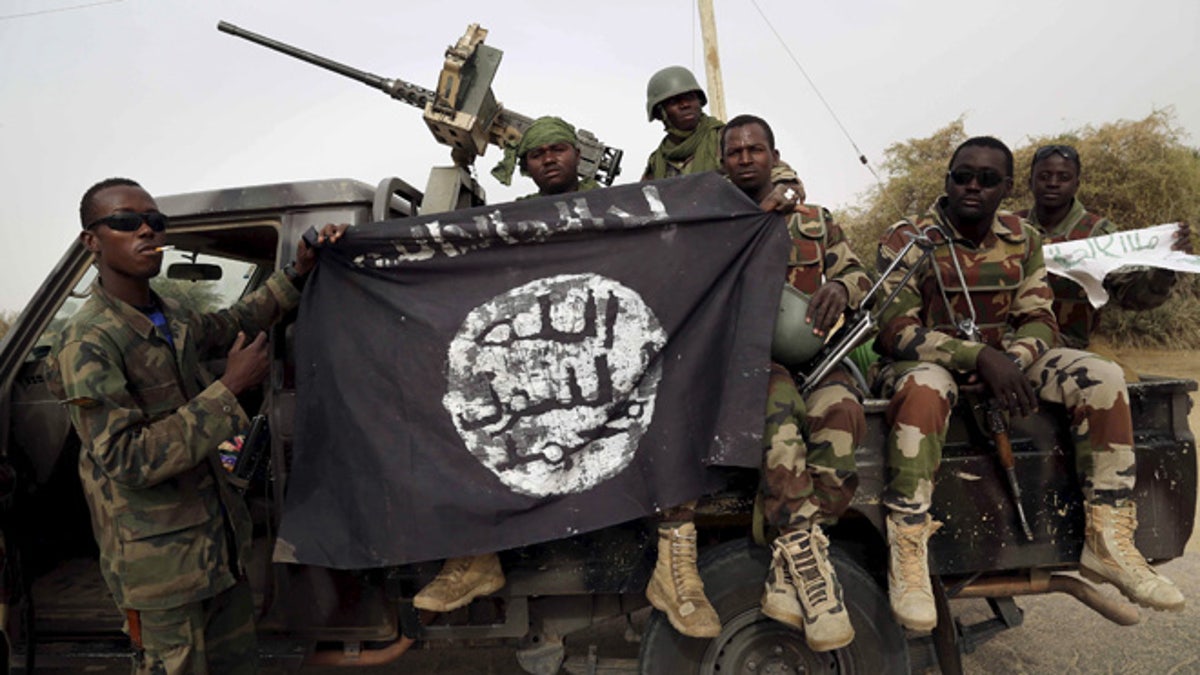 Nigerian soldiers hold up a Boko Haram flag that they had seized in the recently retaken town of Damasak, Nigeria, March 18, 2015. Chadian and Nigerien soldiers took the town from Boko Haram militants earlier this week. The Nigerian army said on Tuesday it had repelled Boko Haram from all but three local government districts in the northeast, claiming victory for its offensive against the Islamist insurgents less than two weeks before a presidential election. Picture taken March 18. REUTERS/Emmanuel Braun - RTR4TZO2