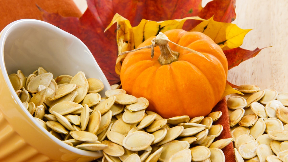 Toasted pumpkin seeds spilling from a yellow bowl