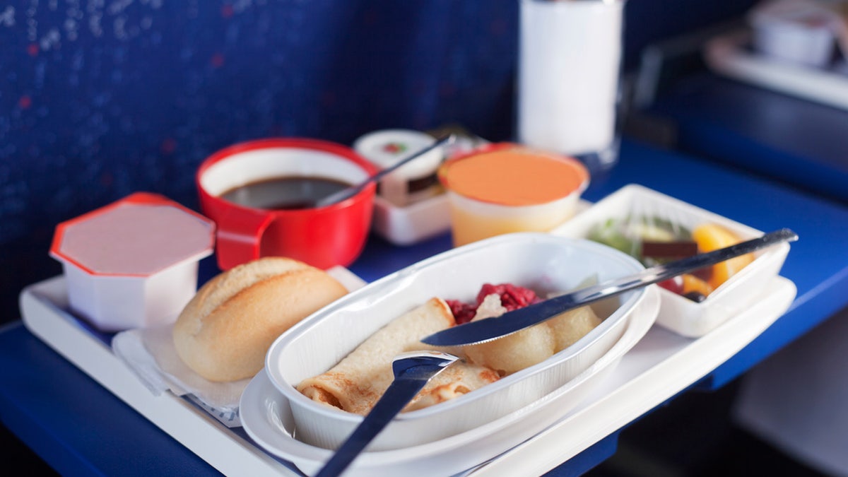 Tray of food on the plane. Focus on a plastic cruet stand with pancakes. Shallow depth of focus.