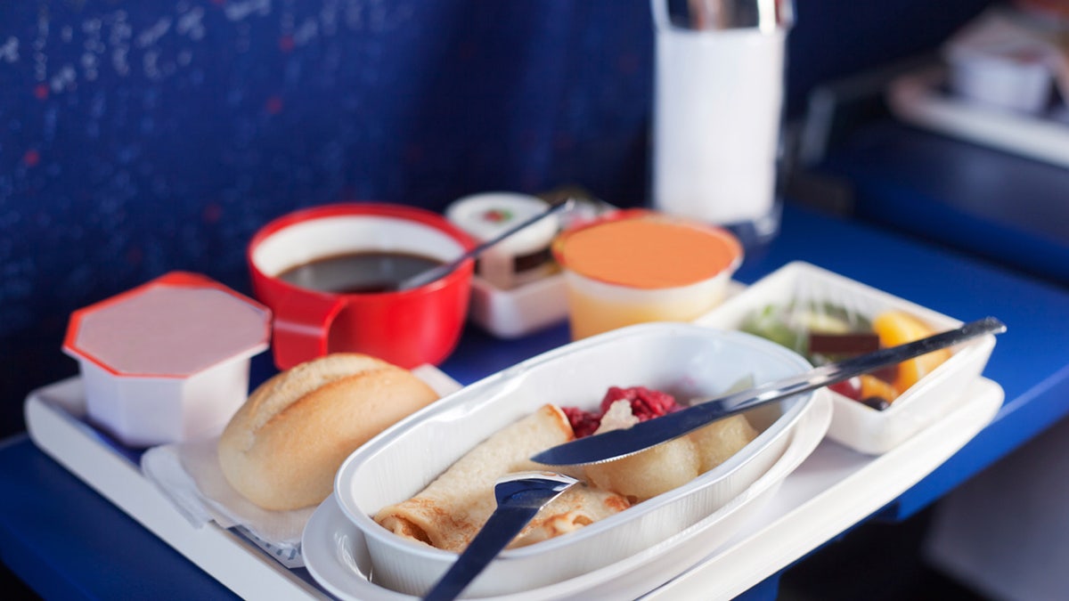 Tray of food on the plane. Focus on a plastic cruet stand with pancakes. Shallow depth of focus.