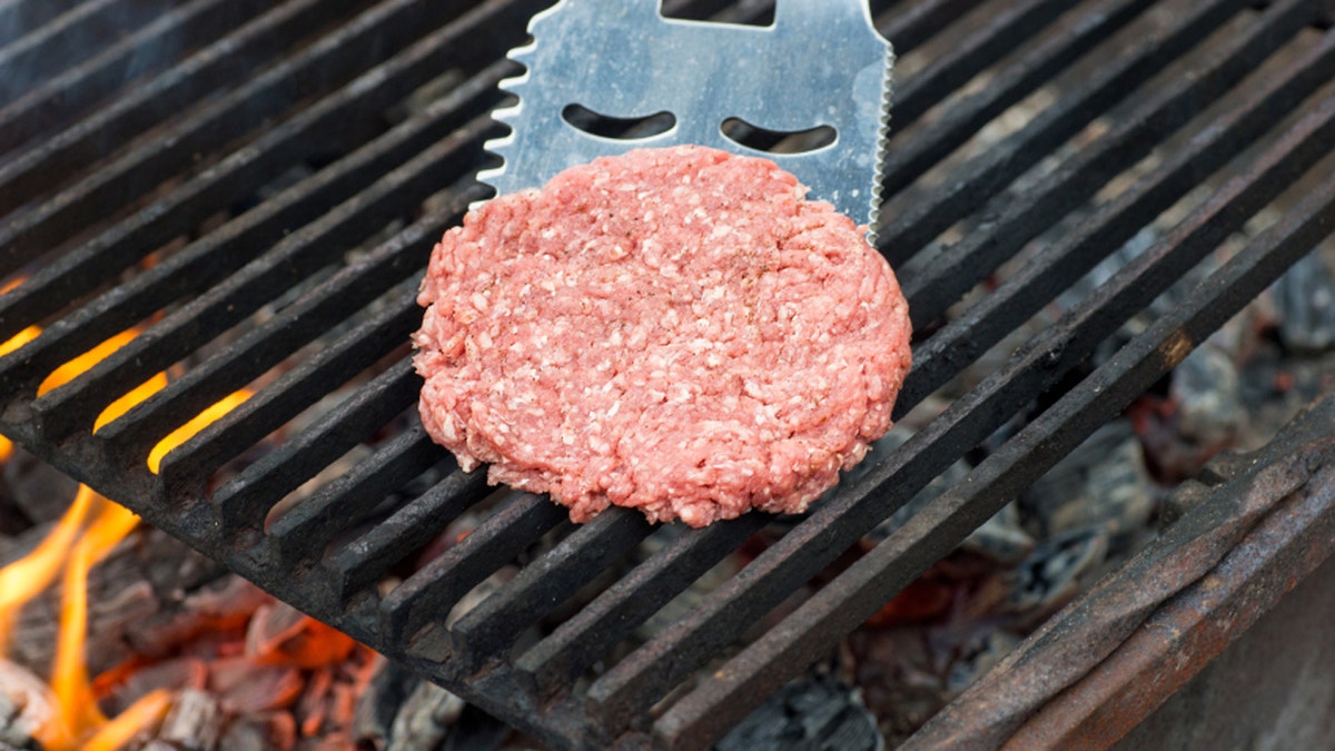 Raw hamburger slice cooking on grill with flames