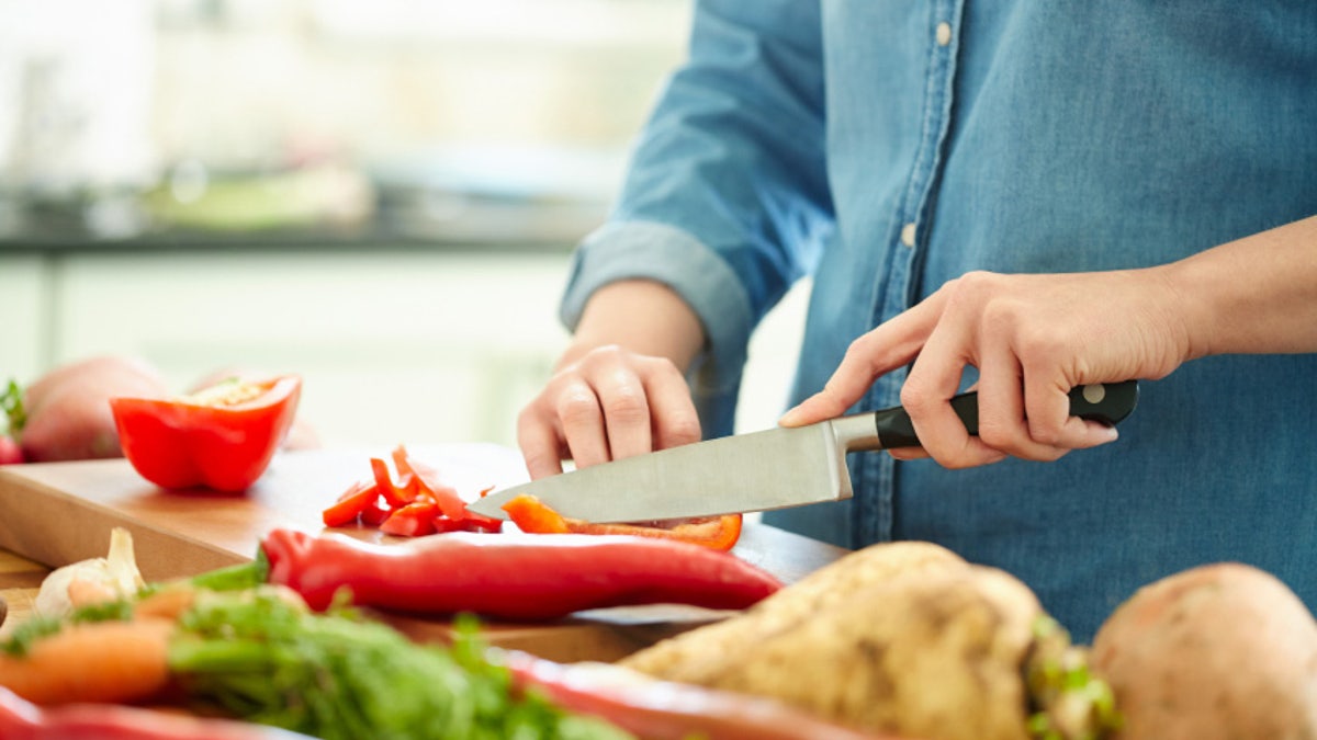 Midsection of woman chopping red bell pepper on wooden board