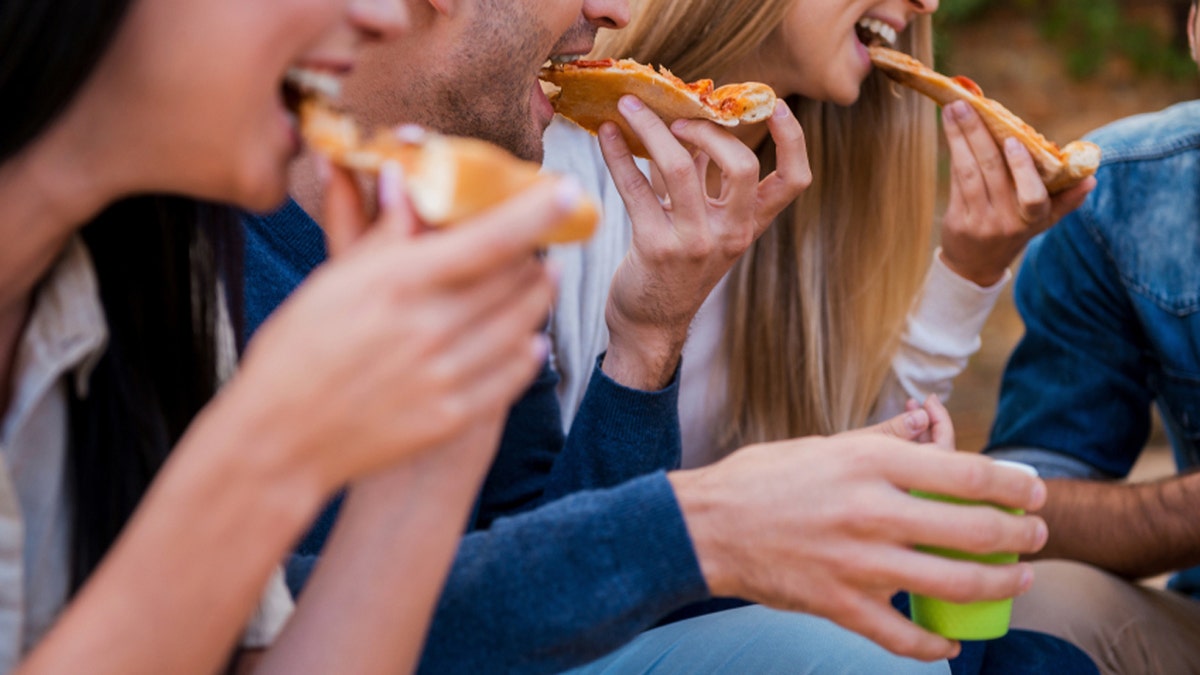 Time for pizza! Group of young people eating pizza while sitting outdoors