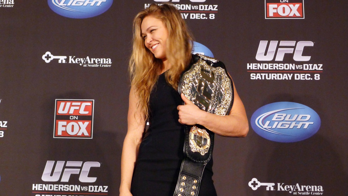 FILE - In this Dec. 6, 2012, file photo, mixed martial arts fighter Ronda Rousey shows off her UFC bantamweight championship belt presented to her by UFC president Dana White during a news conference in Seattle. With her Olympic pedigree and merciless mixed martial arts success, Rousey finally has a showcase worthy of her talent. Rousey and Liz Carmouche are about to make history in the main event at UFC 157 in Anaheim on Saturday, in the first women's bout in the promotion's history. (AP Photo/The Canadian Press, Neil Davidson, File)