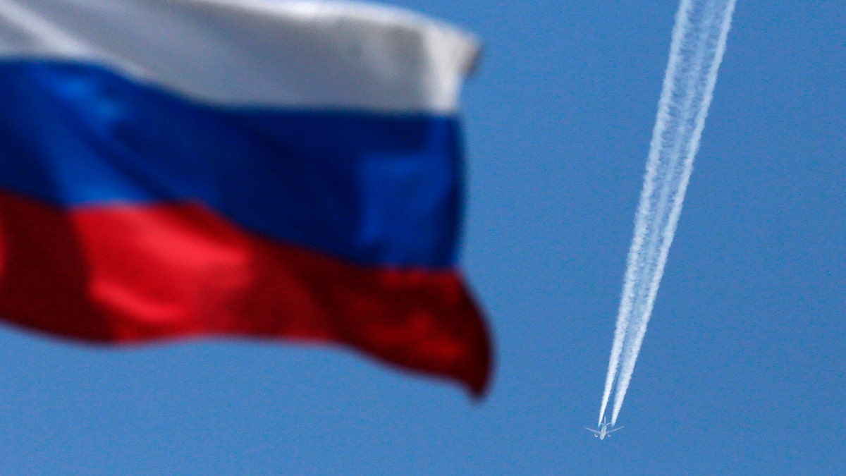 A contrail left by a passenger plane is seen behind a Russian state flag as it passes over the Siberian city of Krasnoyarsk, August 7, 2014. Russian Prime Minister Dmitry Medvedev said on Thursday that Moscow was considering banning transit flights by airlines from the European Union and the United States to the Asia-Pacific region.  REUTERS/Ilya Naymushin (RUSSIA - Tags: POLITICS TRANSPORT BUSINESS) - GM1EA871DC201