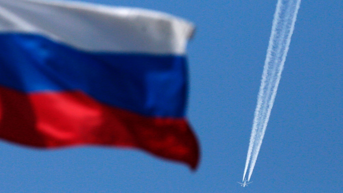 A contrail left by a passenger plane is seen behind a Russian state flag as it passes over the Siberian city of Krasnoyarsk, August 7, 2014. Russian Prime Minister Dmitry Medvedev said on Thursday that Moscow was considering banning transit flights by airlines from the European Union and the United States to the Asia-Pacific region.  REUTERS/Ilya Naymushin (RUSSIA - Tags: POLITICS TRANSPORT BUSINESS) - GM1EA871DC201