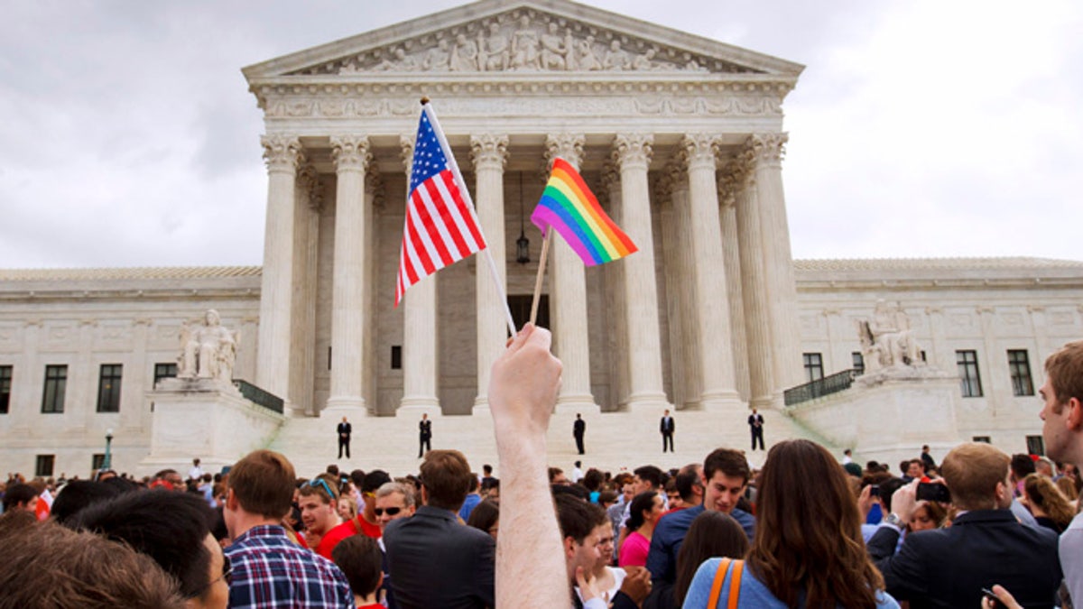 Hands hold up a rainbow flag and US flag during daytime in a crowd