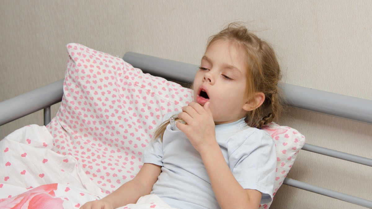 Six year old girl coughs diseased lying in bed with a thermometer on the mouse