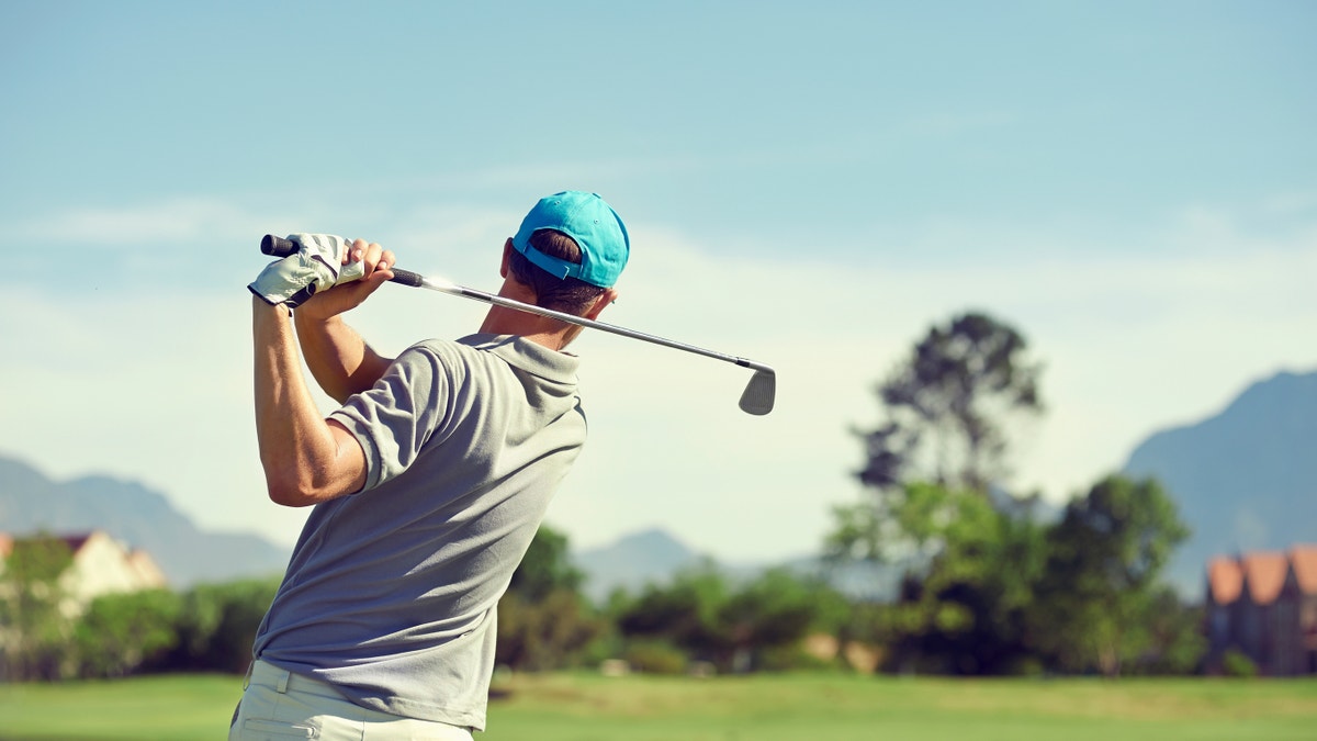 Golfer hitting golf shot with club on course while on summer vacation