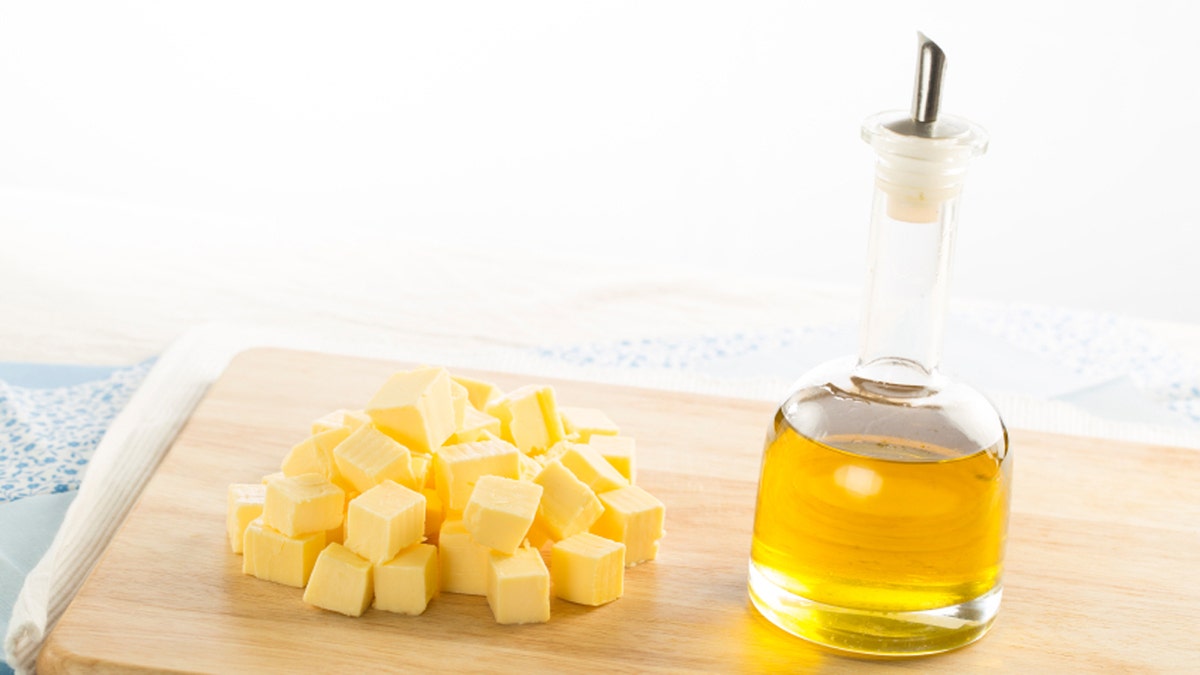 Olive oil in bottle and butter cubes on food preparation surface.
