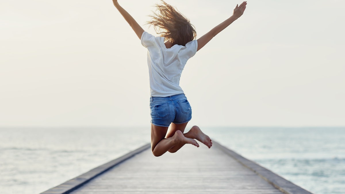 Back view of jumping girl on the pier. Freedom concept