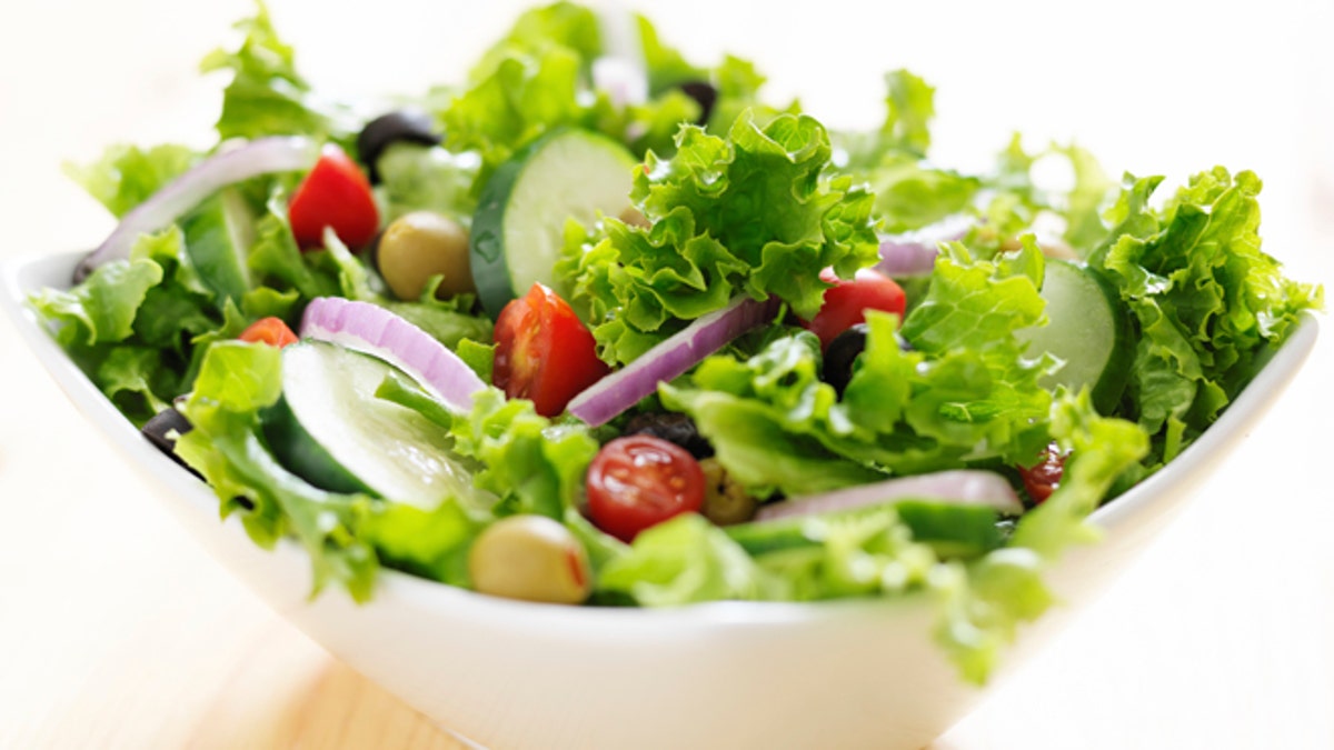 bowl of leafy green salad with olives, tomatoes and cucumber.