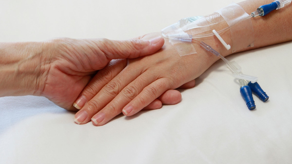 An older person's hand touching the hand of a patient with an intravenous drip