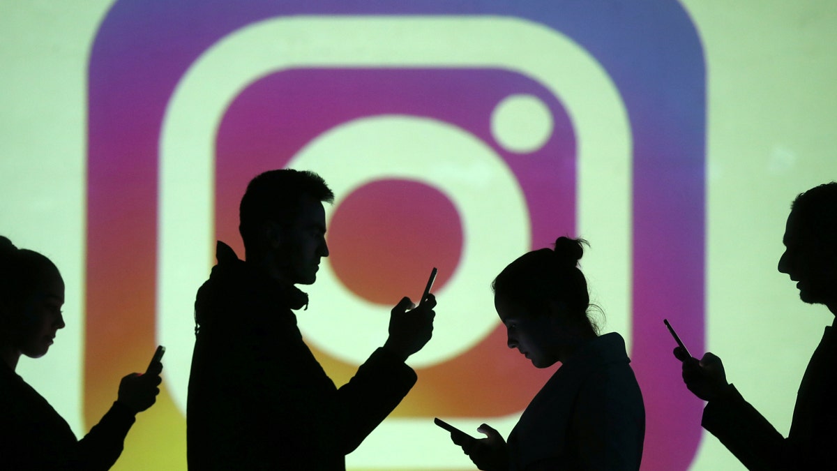 Silhouettes of mobile users are seen next to a screen projection of Instagram logo in this picture illustration taken March 28, 2018.  REUTERS/Dado Ruvic/Illustration - RC1B04777830