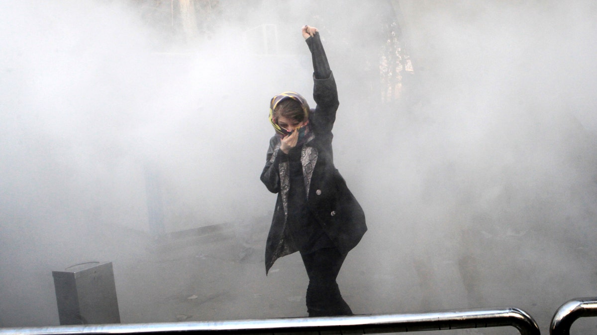 FILE - In this Saturday, Dec. 30, 2017 file photo, taken by an individual not employed by the Associated Press and obtained by the AP outside Iran, a university student attends a protest inside Tehran University while a smoke grenade is thrown by anti-riot Iranian police, in Tehran, Iran. Irans top regional foes, Israel and Saudi Arabia, are both watching that countrys protests for signs they could lead to change. Irans supreme leader has accused enemies of stoking the unrest. (AP Photo, File)