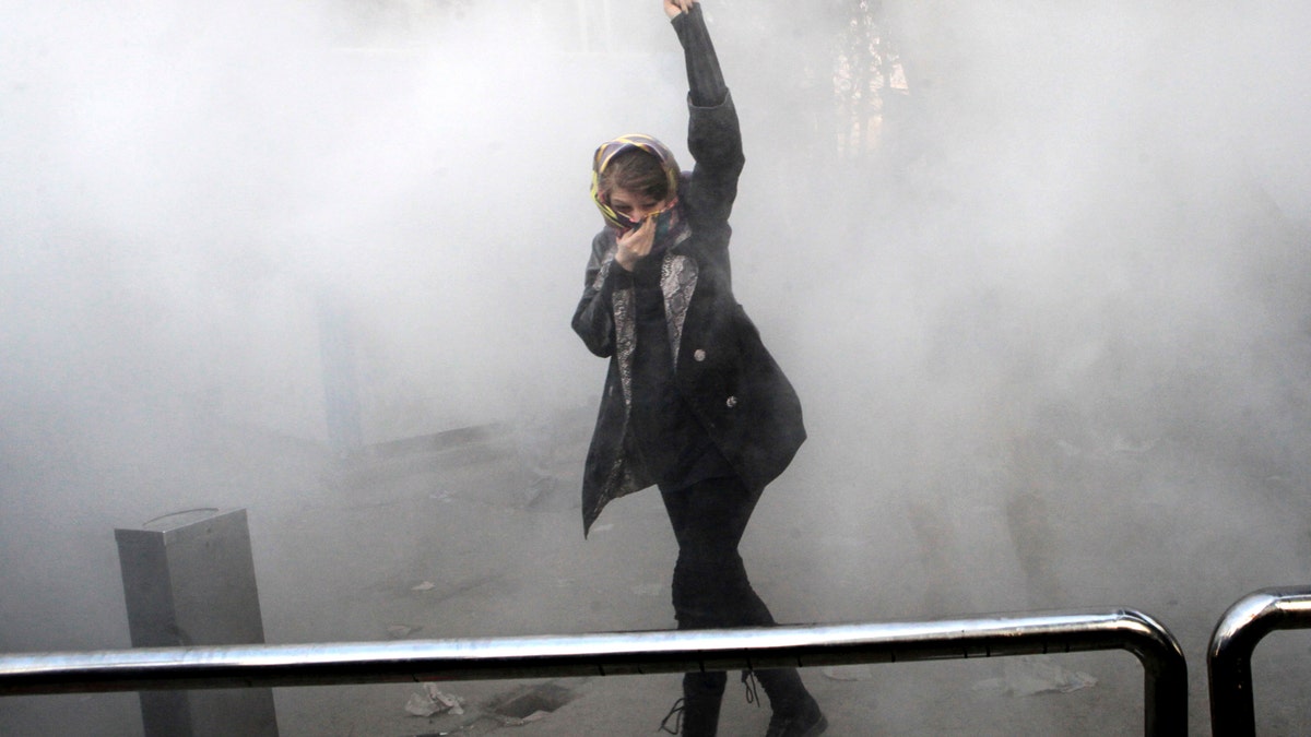 FILE - In this Saturday, Dec. 30, 2017 file photo, taken by an individual not employed by the Associated Press and obtained by the AP outside Iran, a university student attends a protest inside Tehran University while a smoke grenade is thrown by anti-riot Iranian police, in Tehran, Iran. Irans top regional foes, Israel and Saudi Arabia, are both watching that countrys protests for signs they could lead to change. Irans supreme leader has accused enemies of stoking the unrest. (AP Photo, File)