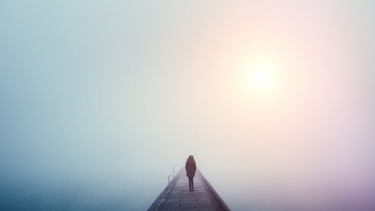 Woman crossing the bridge over lake on a foggy winter day.