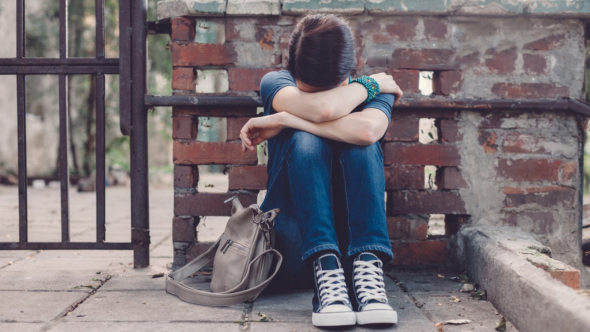 Crying girl with head in hands sitting on the ground