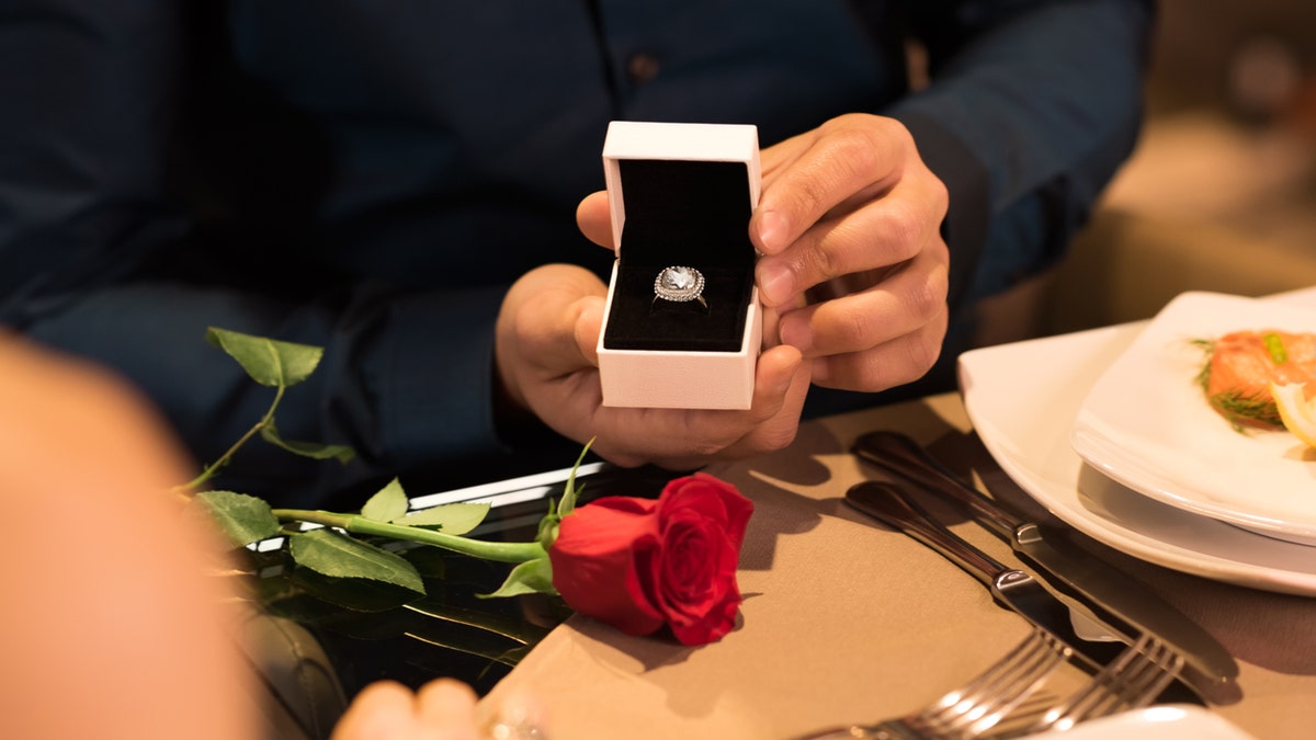 Young man presenting engagement ring to girlfriend. Husband gifting a diamond ring to wife on anniversary. Man holding box with ring making propose to girlfriend.