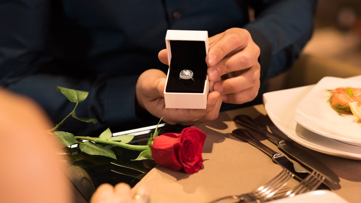 Young man presenting engagement ring to girlfriend. Husband gifting a diamond ring to wife on anniversary. Man holding box with ring making propose to girlfriend.