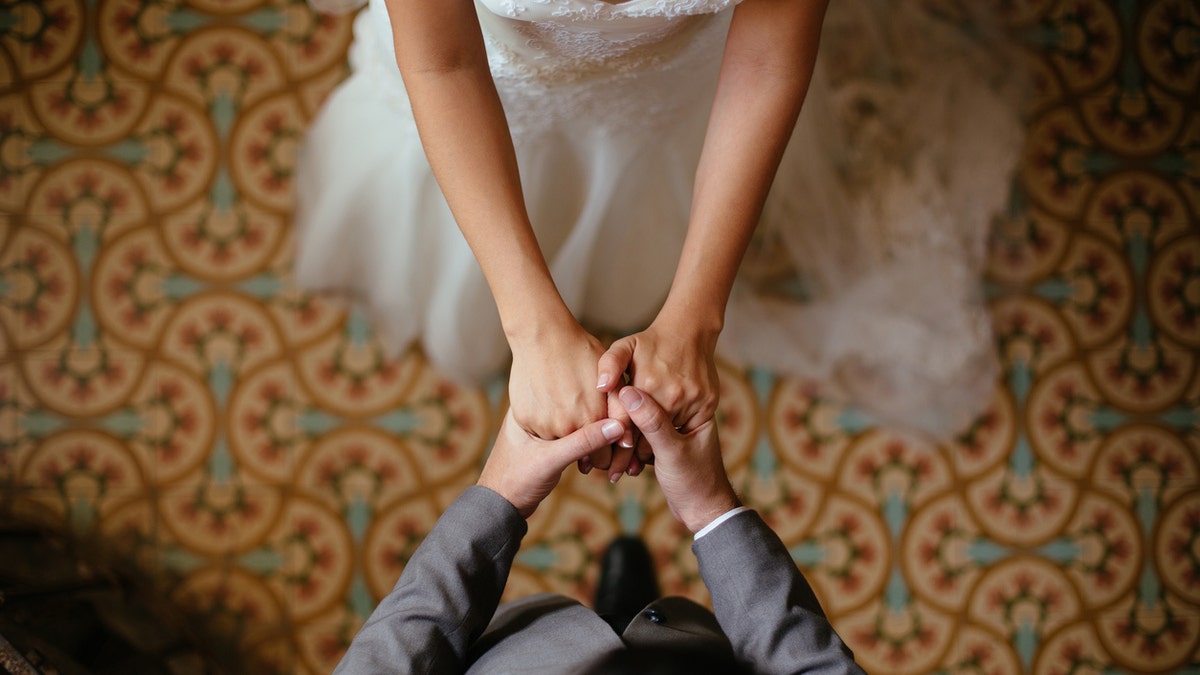 Um close-up de uma noiva e um noivo de mãos dadas a partir de uma vista superior.