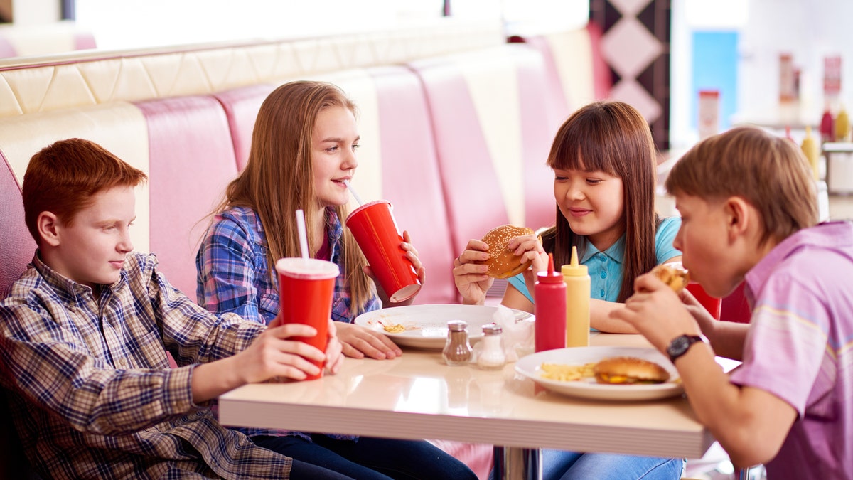 Group of teenage kids eating burgers and drinking cola in fast food restaurant