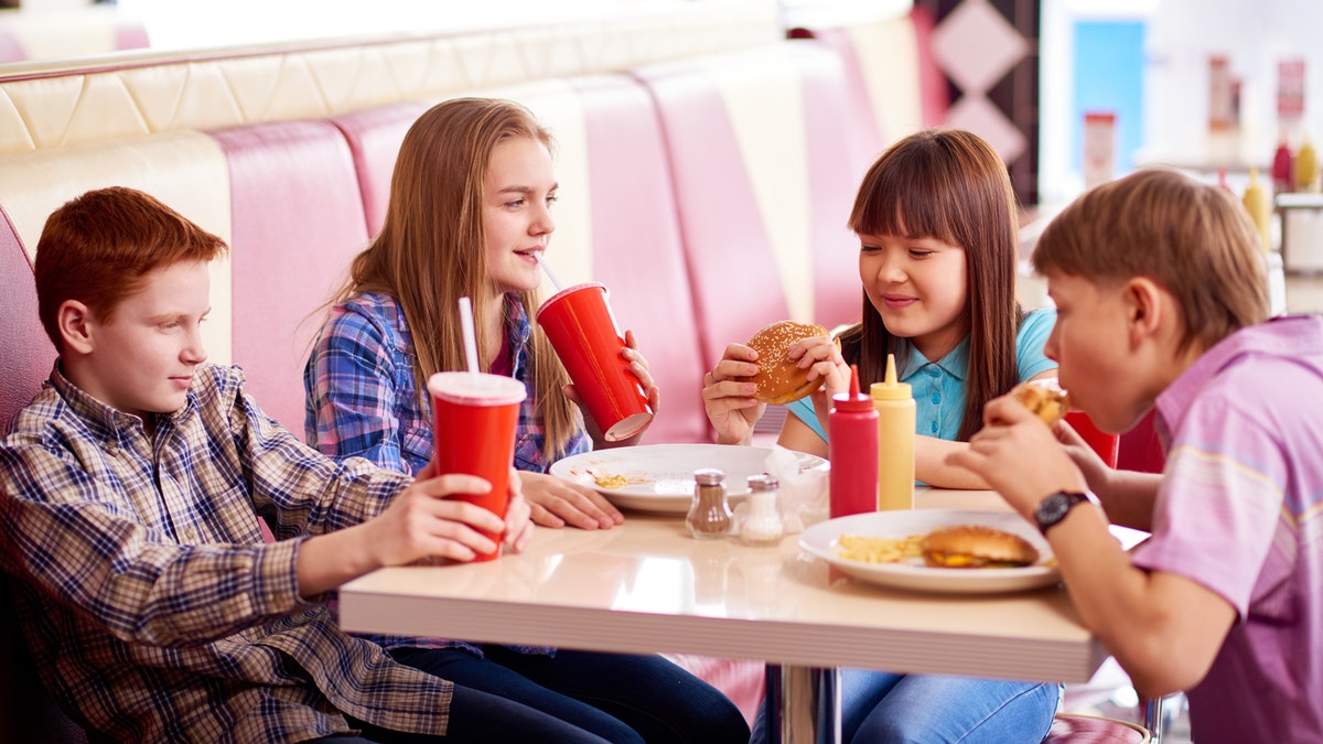 Group of teenage kids eating burgers and drinking cola in fast food restaurant